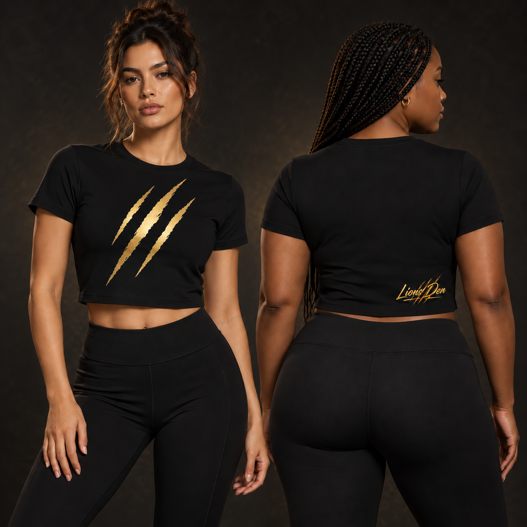 Two women model the black Lions Den claw-mark performance crop tee, showing three antique-gold front slashes and the lower-back script.