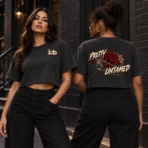 Two women modeling the washed-black Lions Den Crowned LD Pretty Untamed raw-edge crop top, showing the small front LD mark and full back graphic