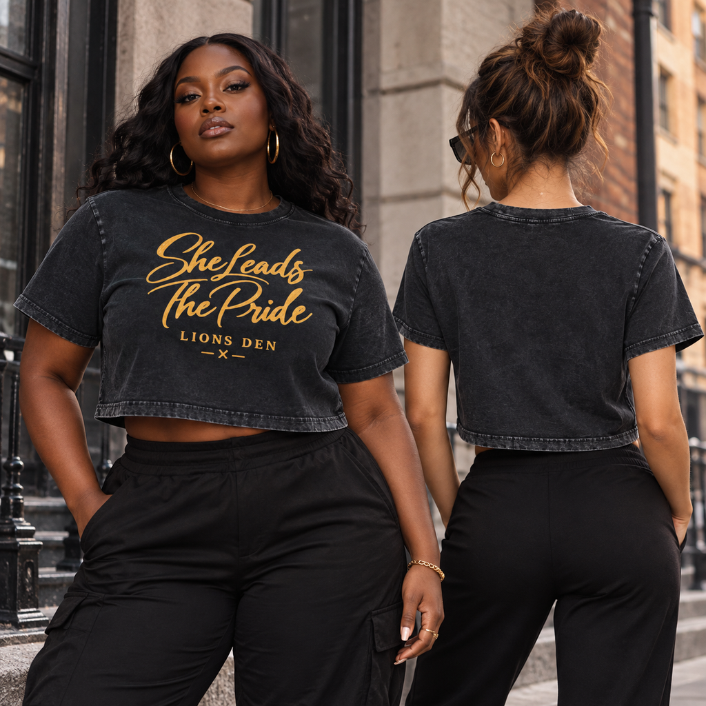 Two women modeling the washed-black Lions Den She Leads The Pride mineral-wash crop tee, showing the front artwork and plain back